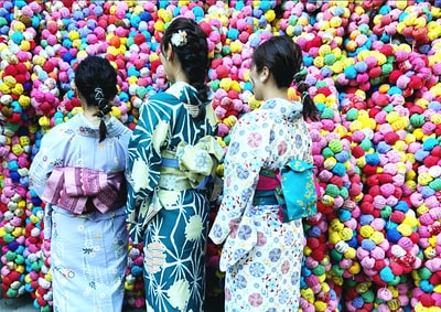 Two women dressed in white, and blue kimono stood beside the colorful balloons
